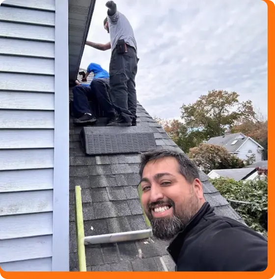 Selfie of a smiling wildlife technician on a roof while teammates perform exclusion repairs.